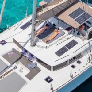 Aerial view of a luxurious Lagoon 450 catamaran sailing in the Athens Riviera with guests relaxing on the sun deck.