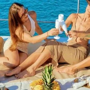 Group of women enjoying drinks and food on a catamaran as it departs from Hersonissos harbor under a sunny sky.