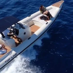 A white speedboat cruises across deep blue water off Mykonos, with several passengers relaxing on board.