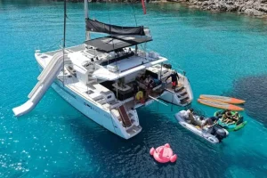 Luxury catamaran anchored in clear blue waters near Elounda, Crete, surrounded by water toys during a cruise stop.