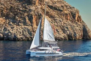 A catamaran sailing on clear blue waters from Hersonissos toward Dia Island under a sunny sky.