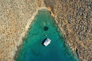 Aerial drone view of a catamaran sailing across turquoise waters in a sheltered island bay.