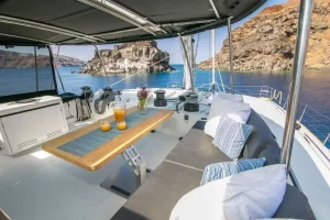 Upper deck of a luxurious Lagoon 620 catamaran featuring a spacious flybridge with plush seating, sun loungers, and panoramic ocean views.