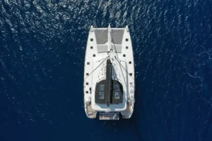 Aerial view of a luxury Lagoon 620 catamaran sailing over the deep blue volcanic waters near Santorini, Greece.